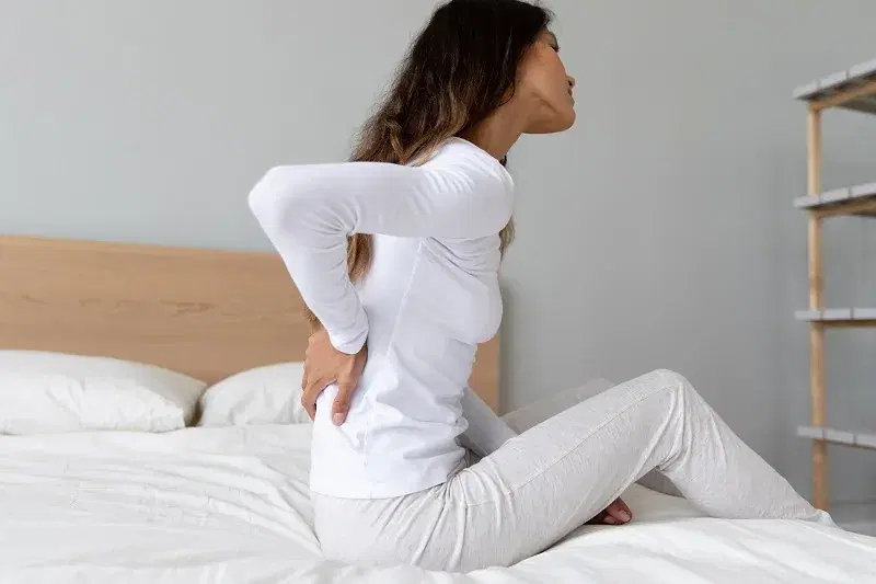 Woman sitting on the edge of a bed with morning back stiffness
